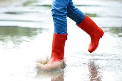 Photo of Woman with red rubber boots running in puddle, closeup. Rainy weather