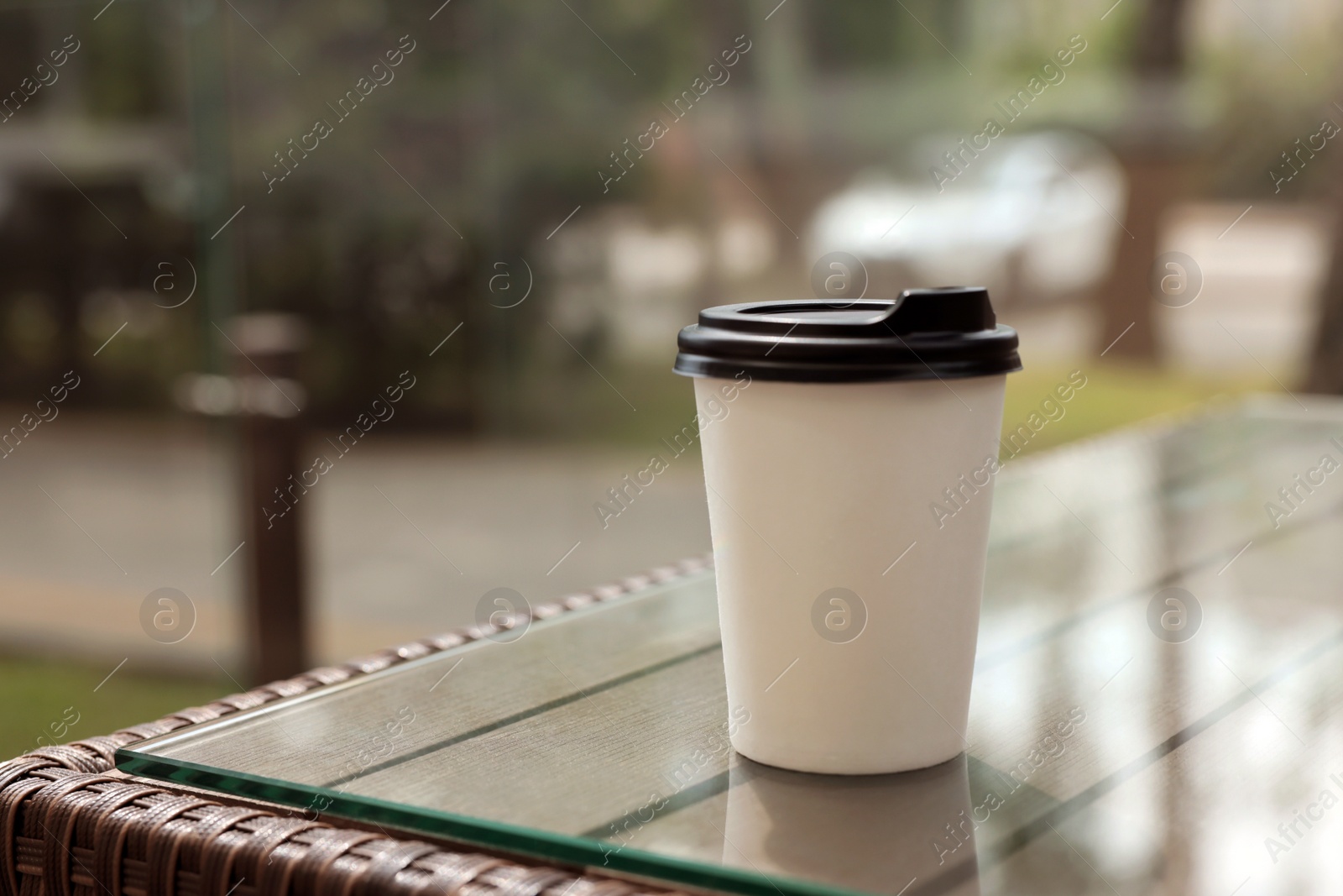 Photo of Paper takeaway cup on glass table outdoors. Coffee to go