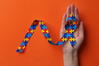 Image of World Autism Awareness Day. Woman with colorful puzzle ribbon on orange background, top view