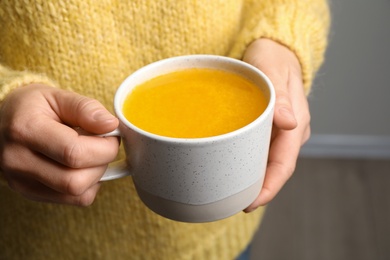 Woman holding cup with sea buckthorn tea on blurred background, closeup