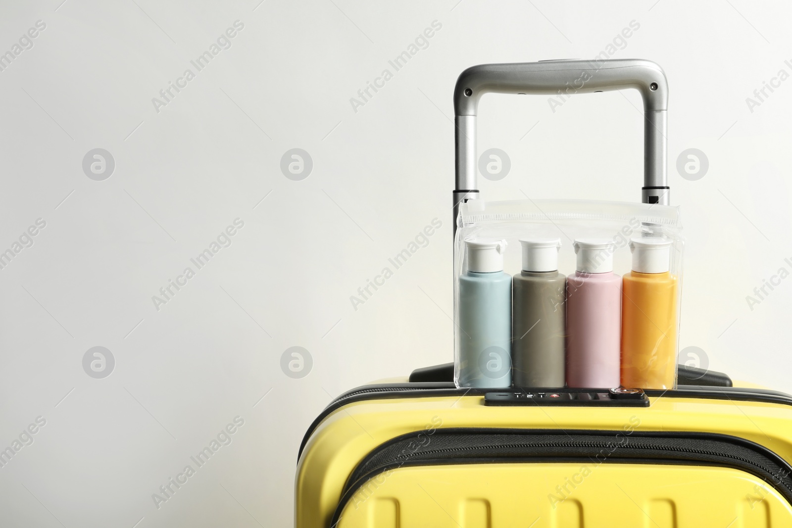 Photo of Cosmetic travel kit in plastic bag on suitcase against light background, space for text