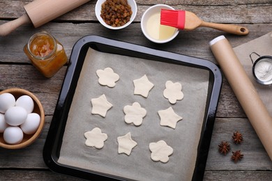 Photo of Parchment paper, baking pan with raw cookies and different ingredients on wooden table, flat lay