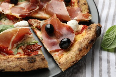 Photo of Tasty pizza with cured ham, olives, mozzarella cheese, sun-dried tomato and basil on table, closeup