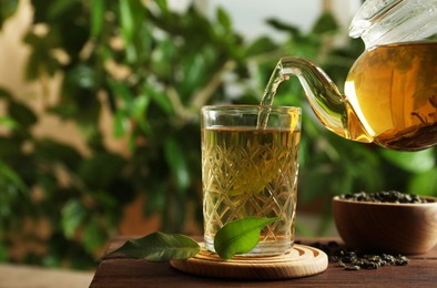 Photo of Pouring green tea into glass on wooden table. Space for text