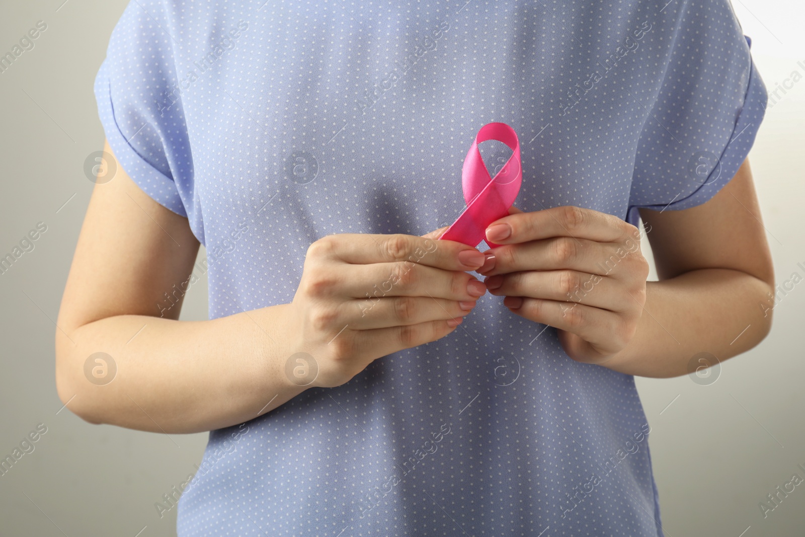 Photo of Woman with pink ribbon on light grey background, closeup. Breast cancer awareness