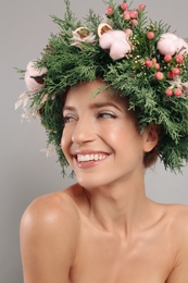 Happy young woman wearing wreath on grey background