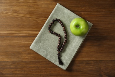 Photo of Rosary beads and apple on wooden table, top view. Lent season