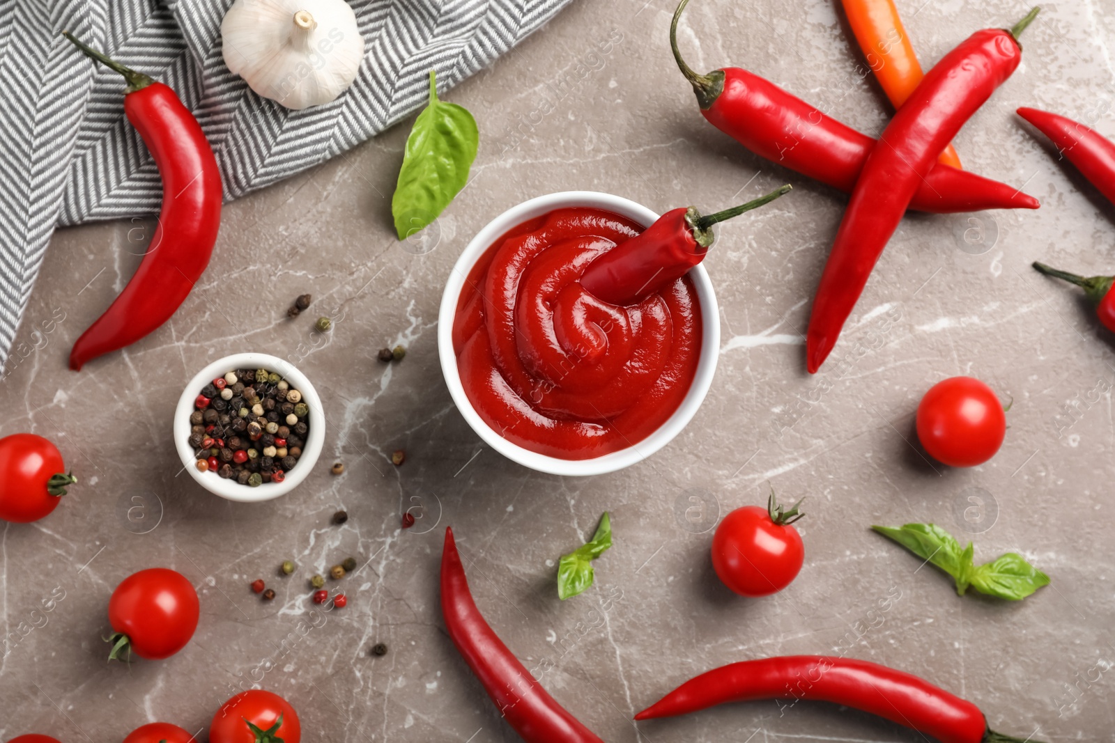 Photo of Flat lay composition with bowl of spicy chili sauce and fresh peppers on gray background