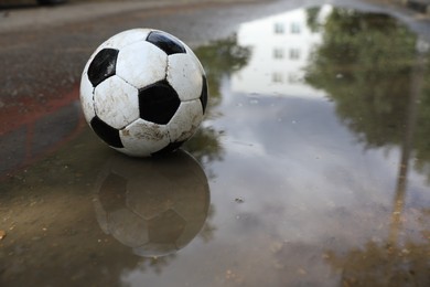 Photo of Dirty soccer ball near puddle outdoors, space for text