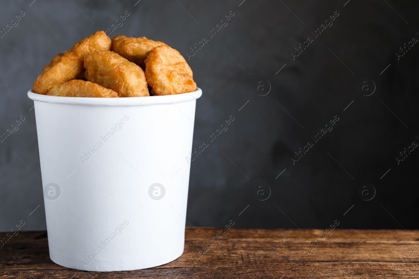 Photo of Bucket with delicious chicken nuggets on wooden table. Space for text