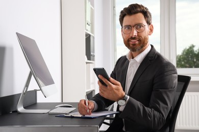 Photo of Handsome businessman using smartphone at workplace in office
