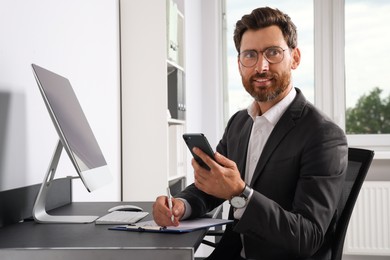 Handsome businessman using smartphone at workplace in office