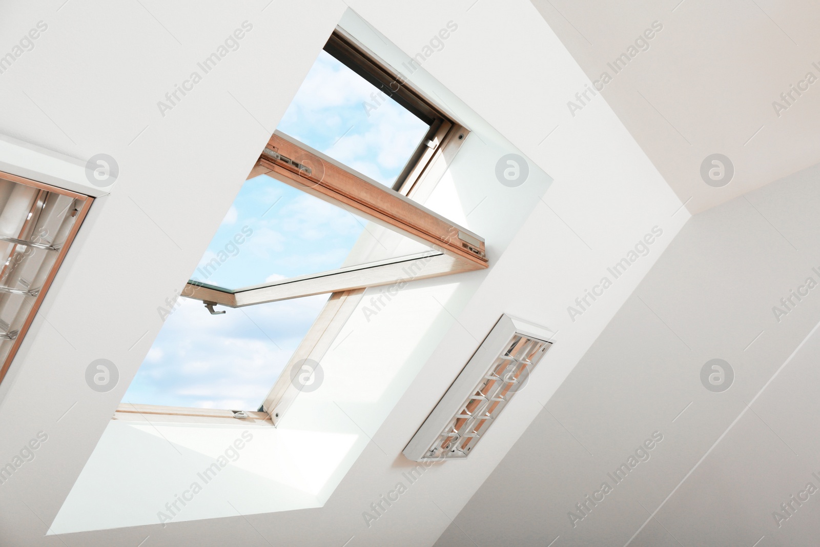 Photo of Open skylight roof window on slanted ceiling in attic room, low angle view