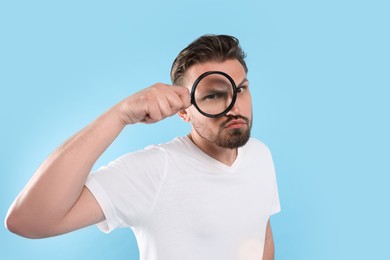 Photo of Handsome man looking through magnifier on light blue background