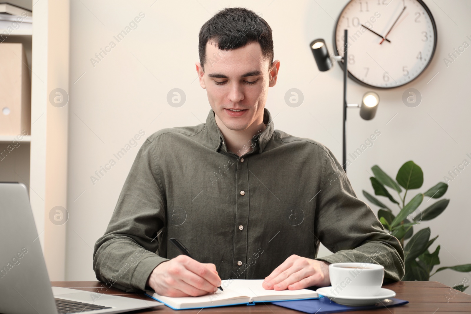 Photo of Man taking notes at wooden table in office