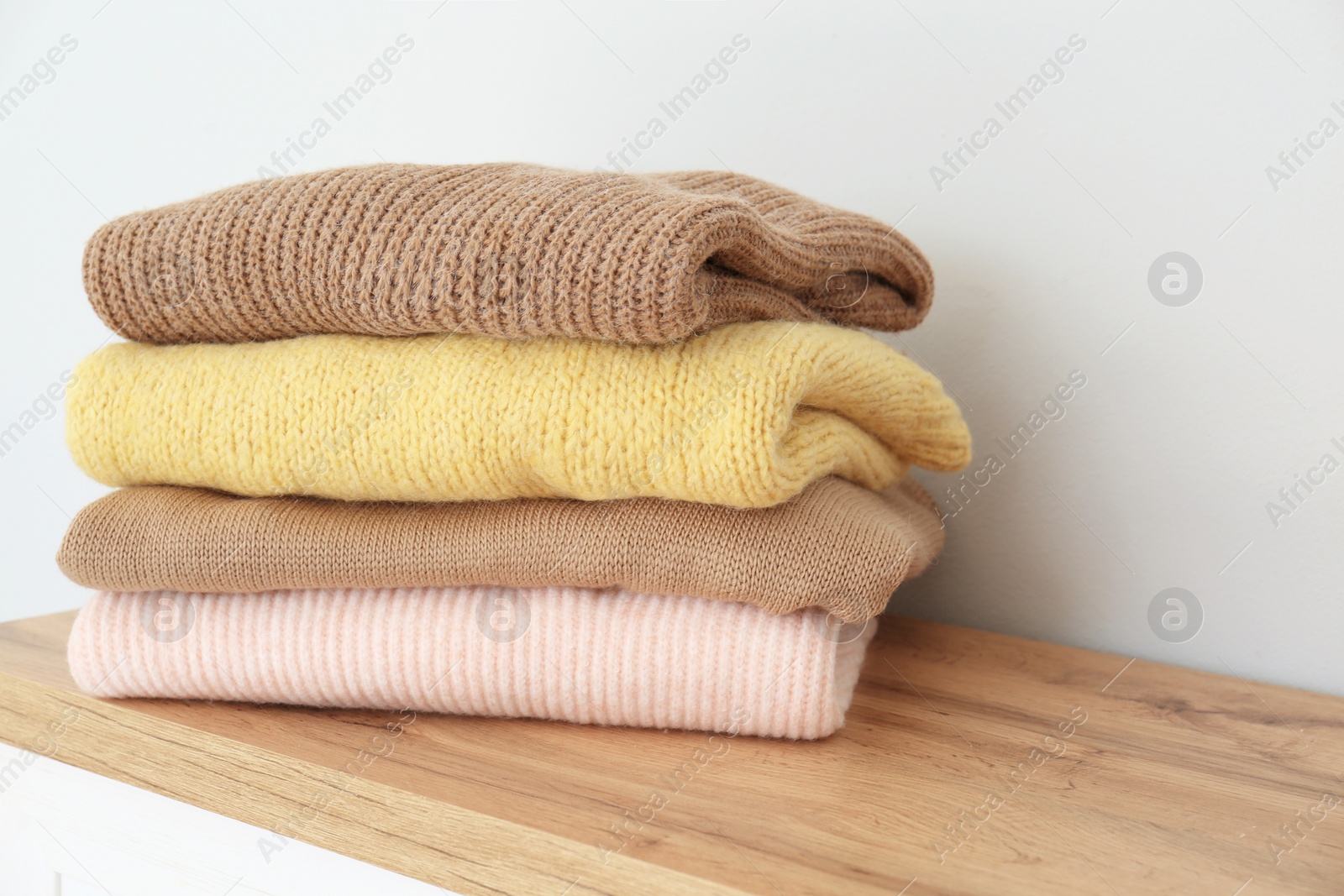 Photo of Stack of folded warm knitted sweaters on wooden table