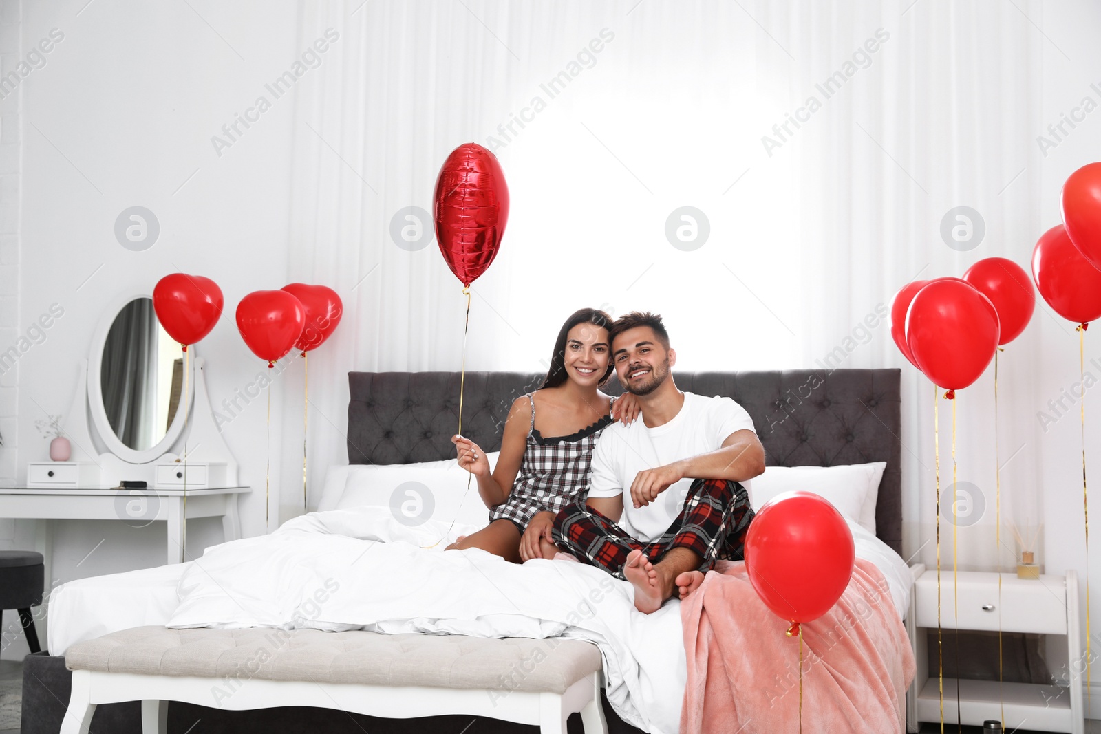 Photo of Young couple in bedroom decorated with air balloons. Celebration of Saint Valentine's Day