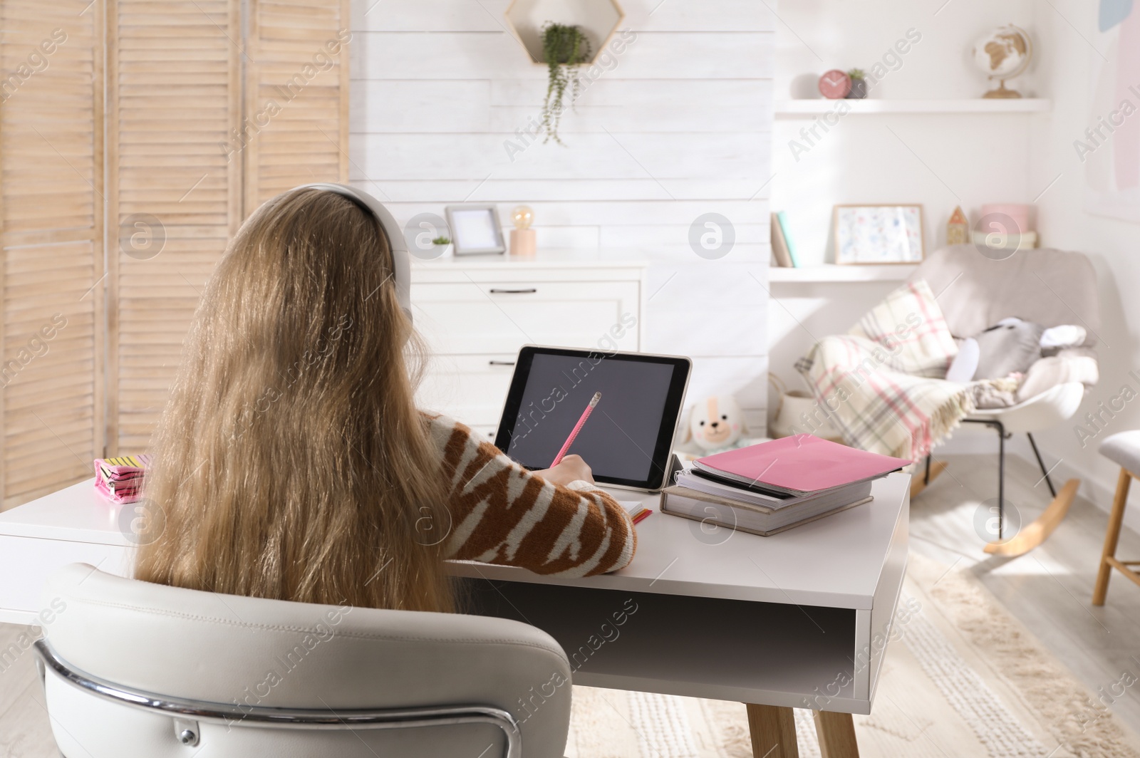 Photo of Cute little girl with modern tablet studying online at home, back view. E-learning