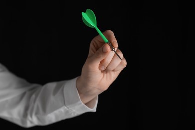 Businesswoman holding green dart on black background, closeup