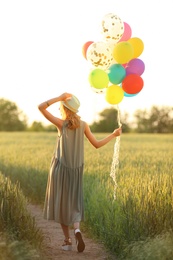 Photo of Young woman with colorful balloons in field on sunny day