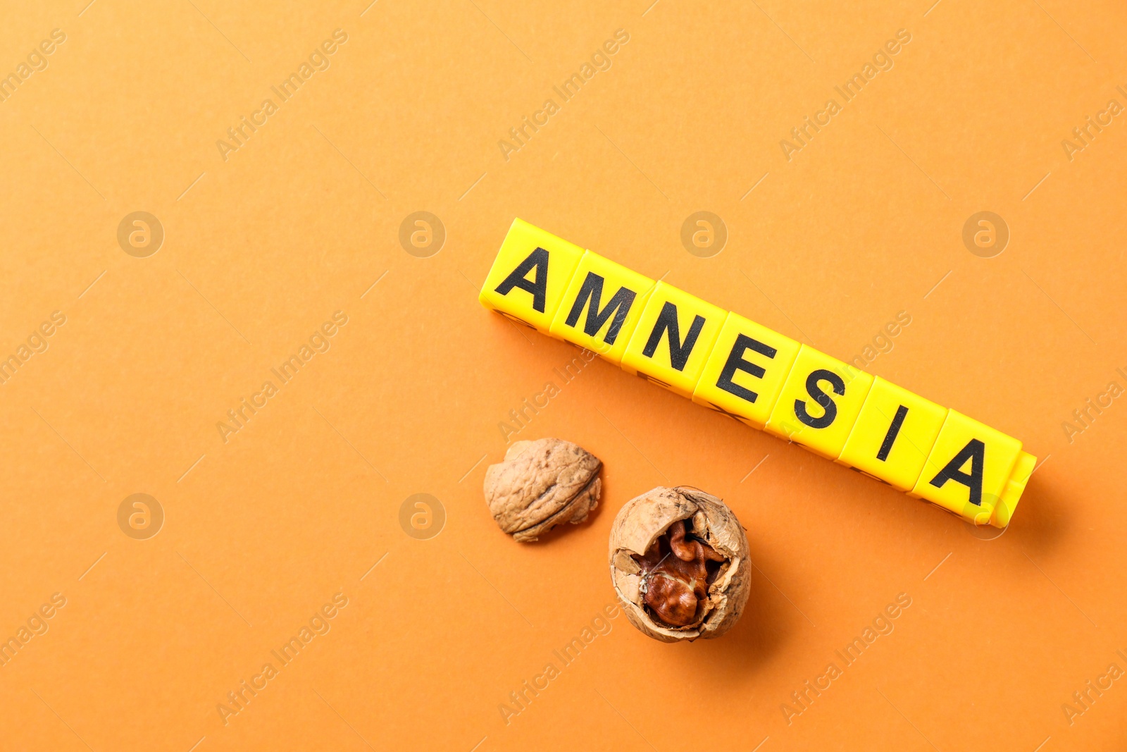 Photo of Word Amnesia made of yellow cubes and broken walnut on orange background, flat lay. Space for text