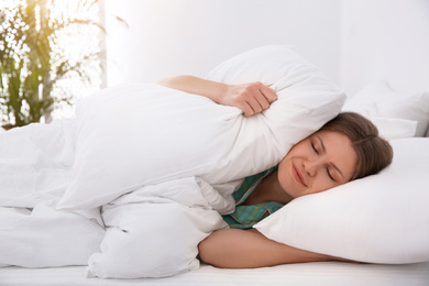 Sleepy young woman covering ears with pillows at home in morning