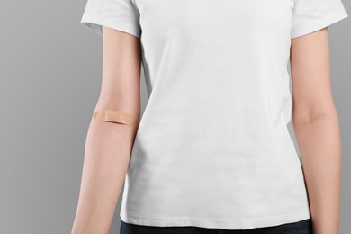 Photo of Blood donation concept. Woman with adhesive plaster on arm against grey background, closeup