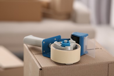 Photo of Dispenser with roll of adhesive tape on box indoors, closeup. Space for text