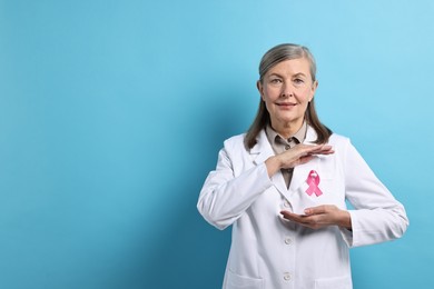 Photo of Mammologist with pink ribbon on light blue background, space for text. Breast cancer awareness