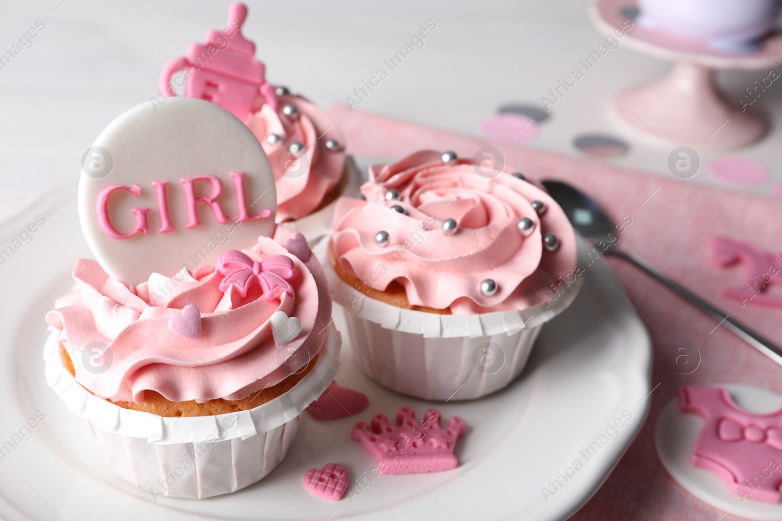 Photo of Delicious cupcakes with pink cream and toppers for baby shower on plate, closeup