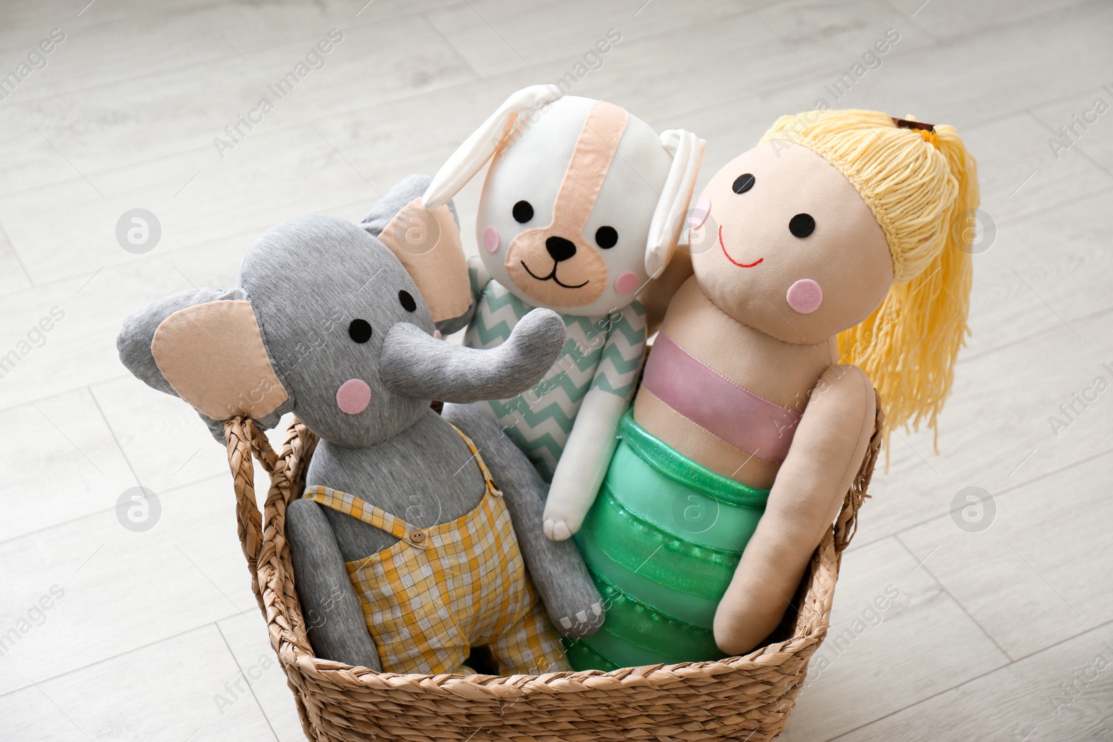 Photo of Funny toy elephant, dog and doll in basket on floor. Decor for children's room interior