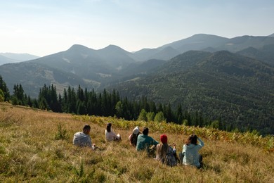 Image of Group of tourists sitting on hill in mountains, back view