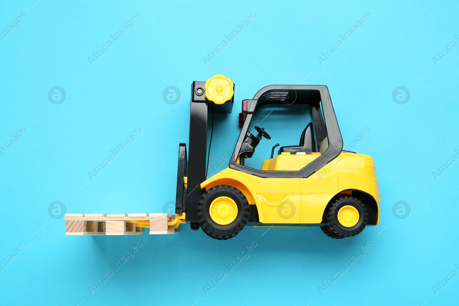 Photo of Toy forklift with wooden pallet on light blue background, top view