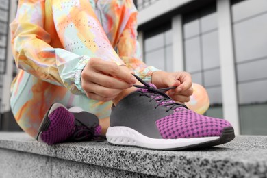 Photo of Woman in gym clothes tying shoelace of sneakers on street, closeup