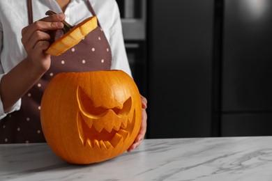 Photo of Woman with carved pumpkin for Halloween at white marble table in kitchen, closeup. Space for text