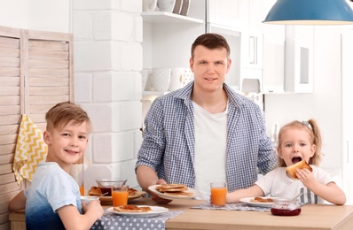 Photo of Father and cute little children having breakfast with tasty toasted bread at table