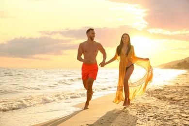 Happy young couple running together on beach at sunset