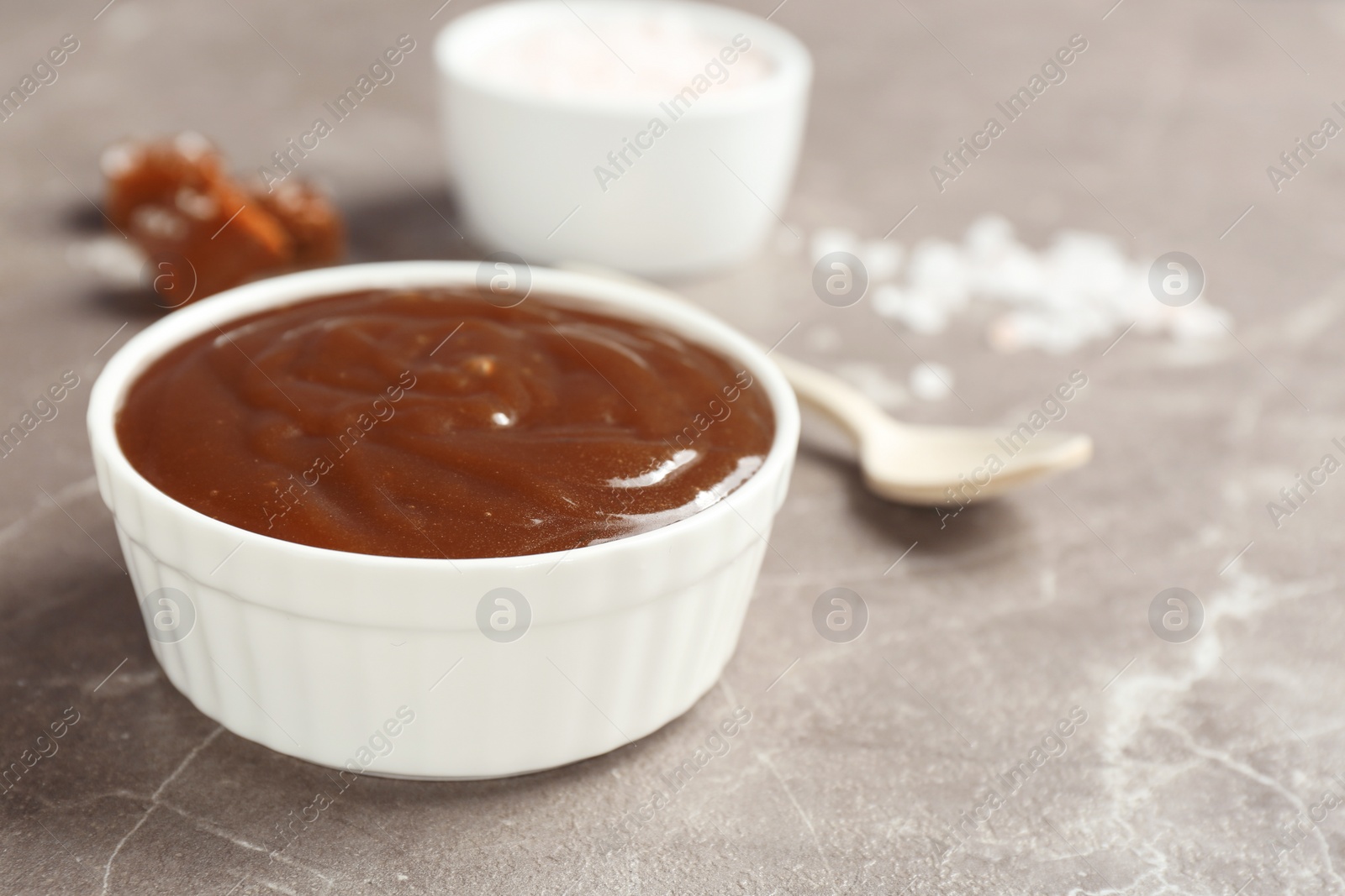 Photo of Bowl with tasty caramel sauce on grey table. Space for text