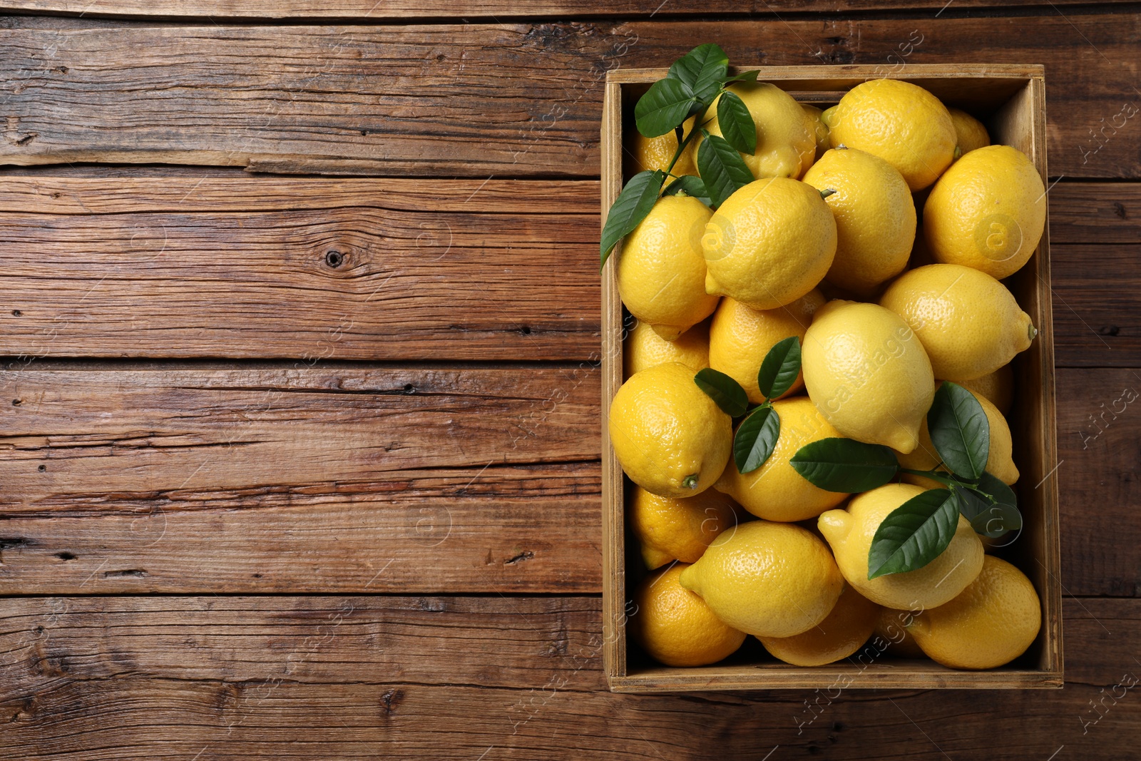 Photo of Fresh lemons in crate on wooden table, top view. Space for text