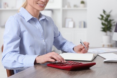 Professional accountant using calculator at wooden desk in office, closeup