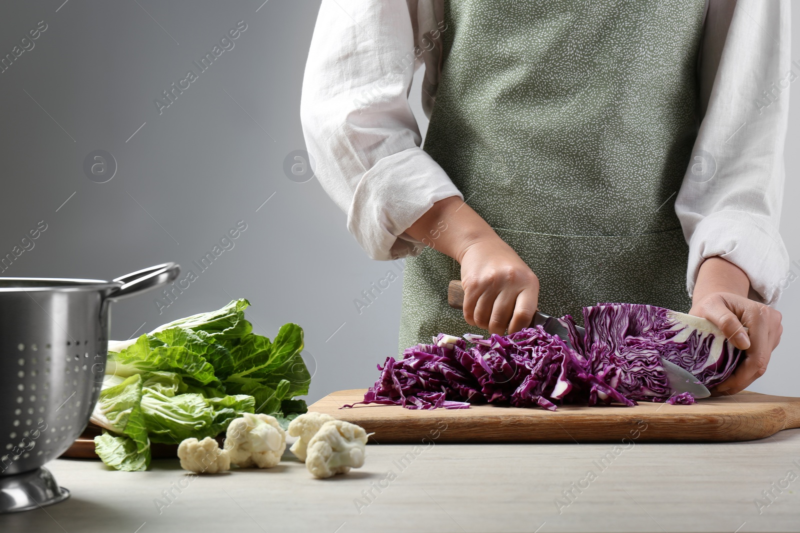 Photo of Woman cutting fresh radicchio cabbage on board at wooden table, closeup