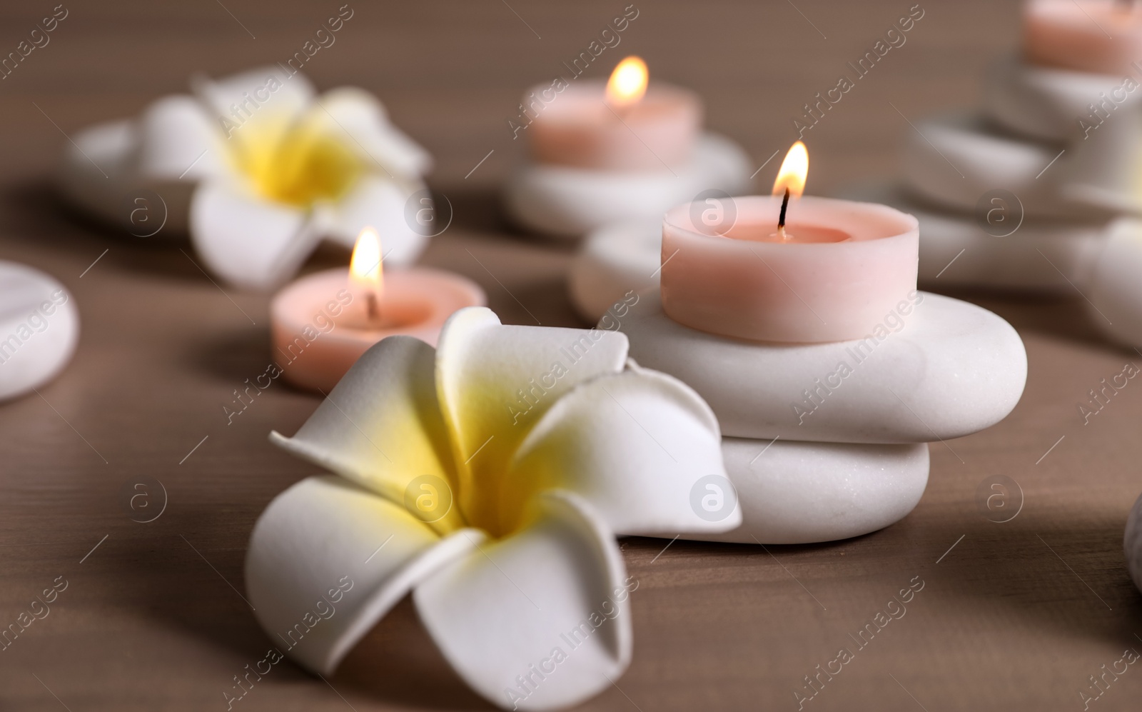 Photo of Spa stones, flowers and burning candles on wooden table