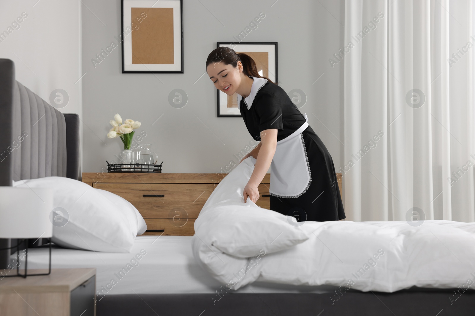 Photo of Young chambermaid making bed in hotel room