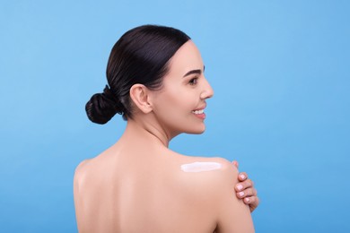 Photo of Beautiful woman with smear of body cream on her shoulder against light blue background, back view