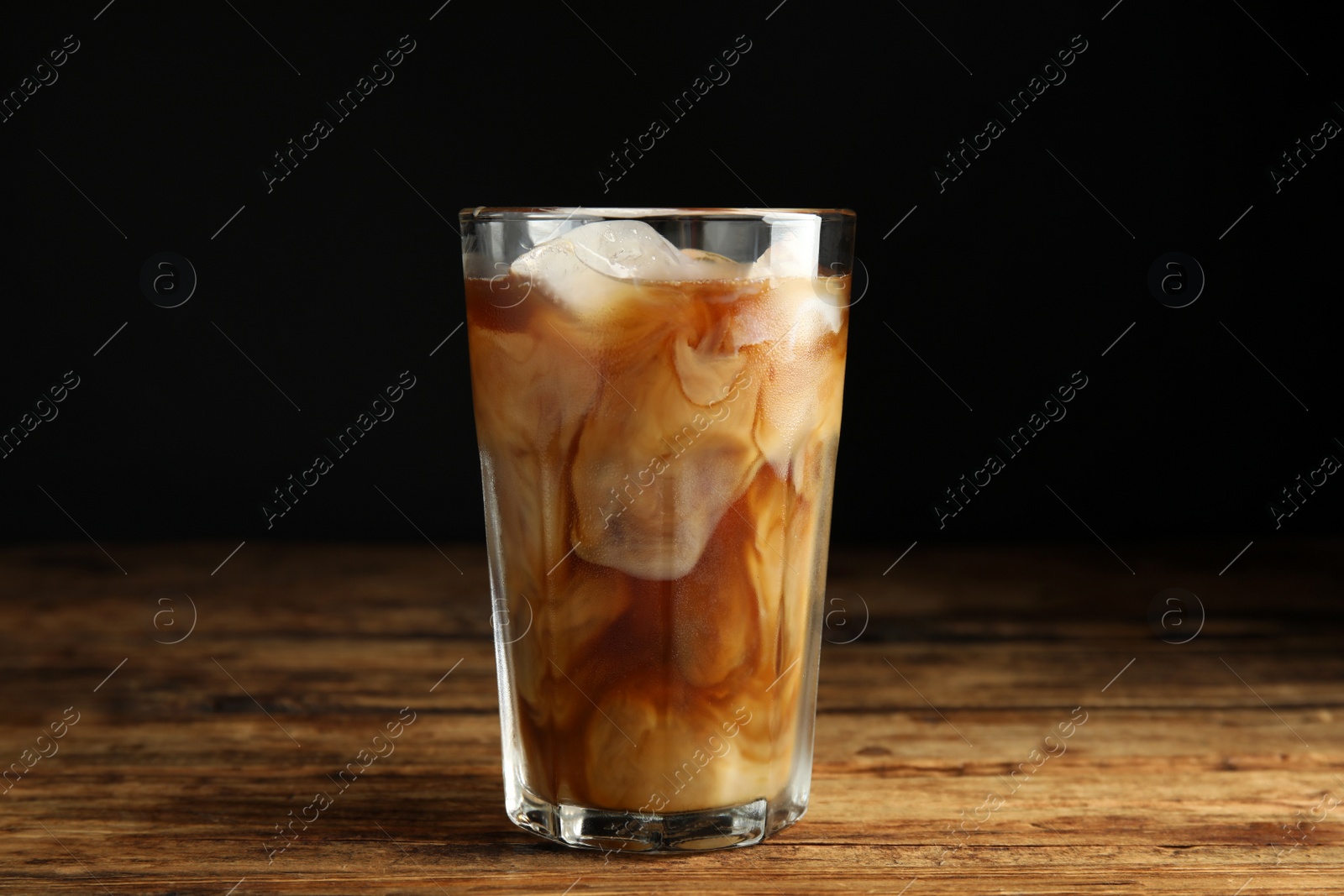 Photo of Glass of coffee with milk and ice cubes on wooden table