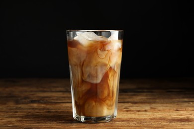 Glass of coffee with milk and ice cubes on wooden table