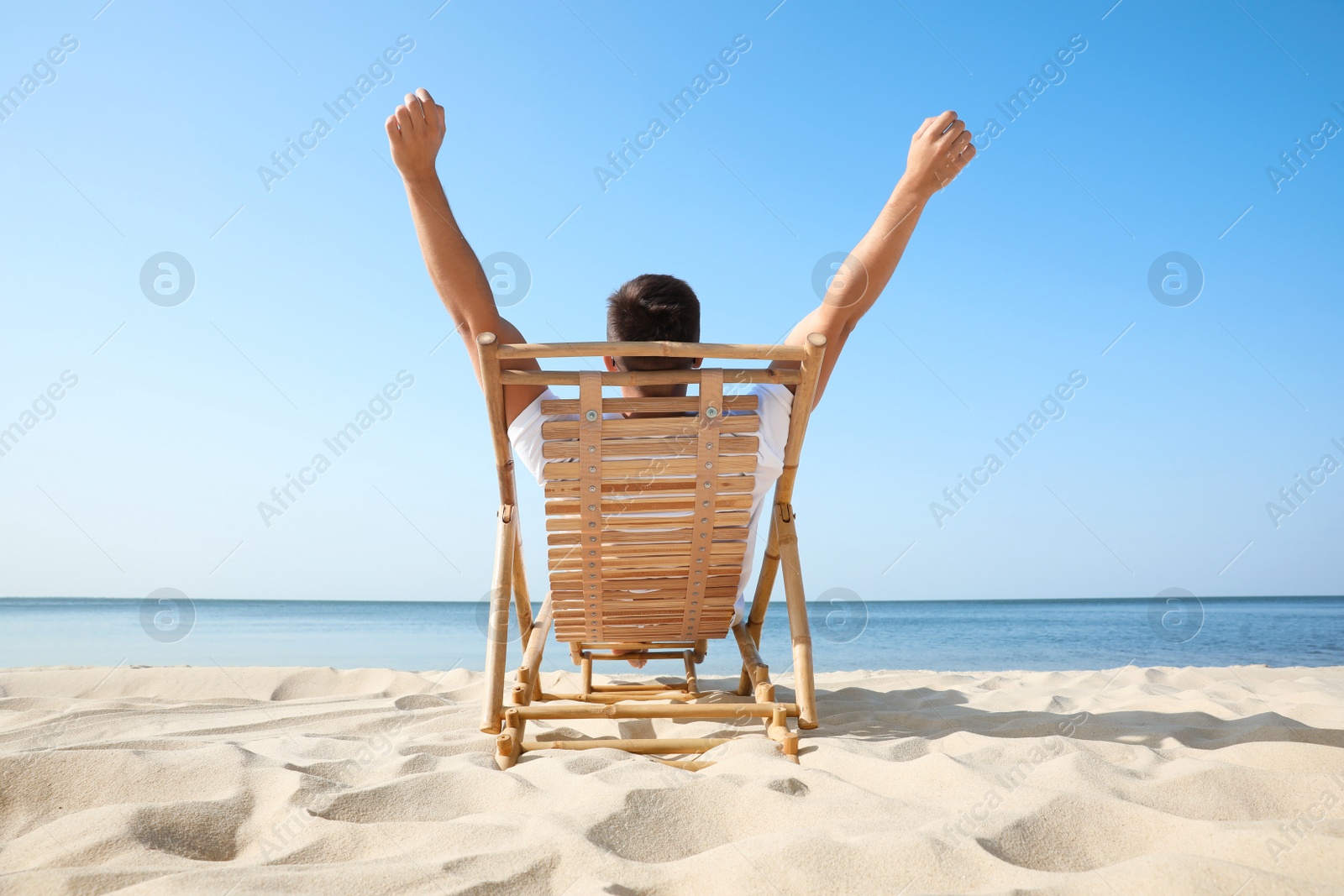 Photo of Young man relaxing in deck chair on sandy beach