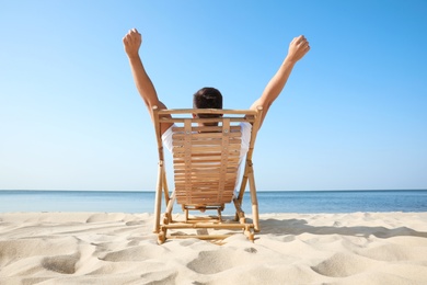 Young man relaxing in deck chair on sandy beach