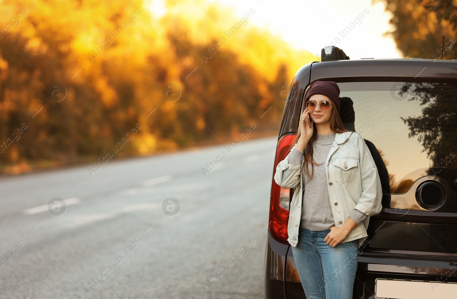 Photo of Young woman with mobile phone near car on country road. Space for text