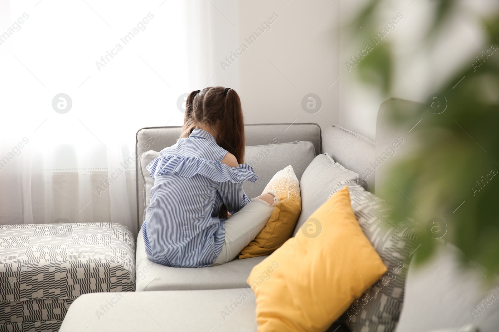Photo of Little girl sitting on sofa in living room. Autism concept
